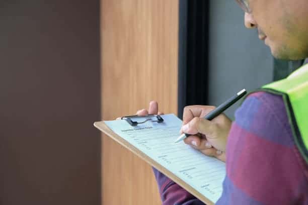 A man in a vest writing on a clipboard.