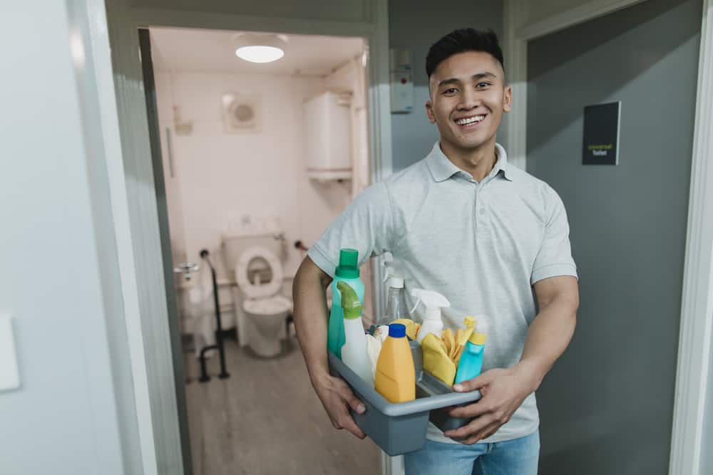 A man holding a basket of cleaning supplies in a hallway.