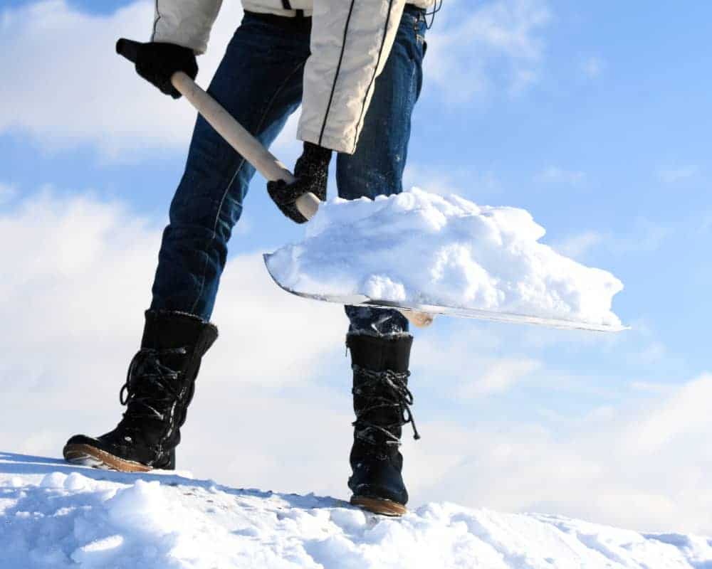 A person holding a snow shovel on top of a snowy hill.