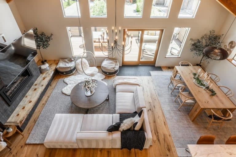 Modern open-concept living and dining area with a white sectional sofa, round coffee table, fireplace, wood floors, large windows, and a wooden dining table with chairs.